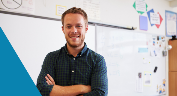 Photo of a male secondary school teacher in the classroom with a whiteboard, shelving and posters seen behind him