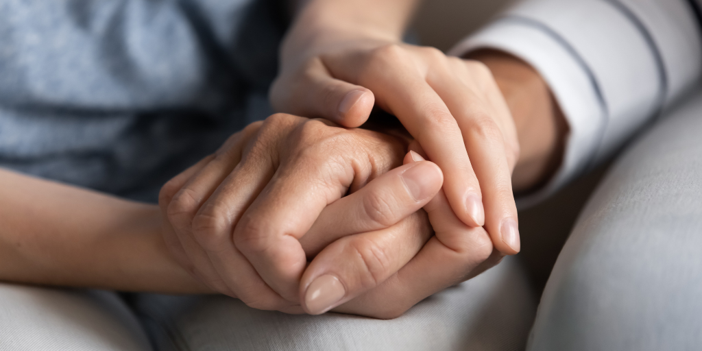 This is an image of an older adult holding a young person's hand in comfort.